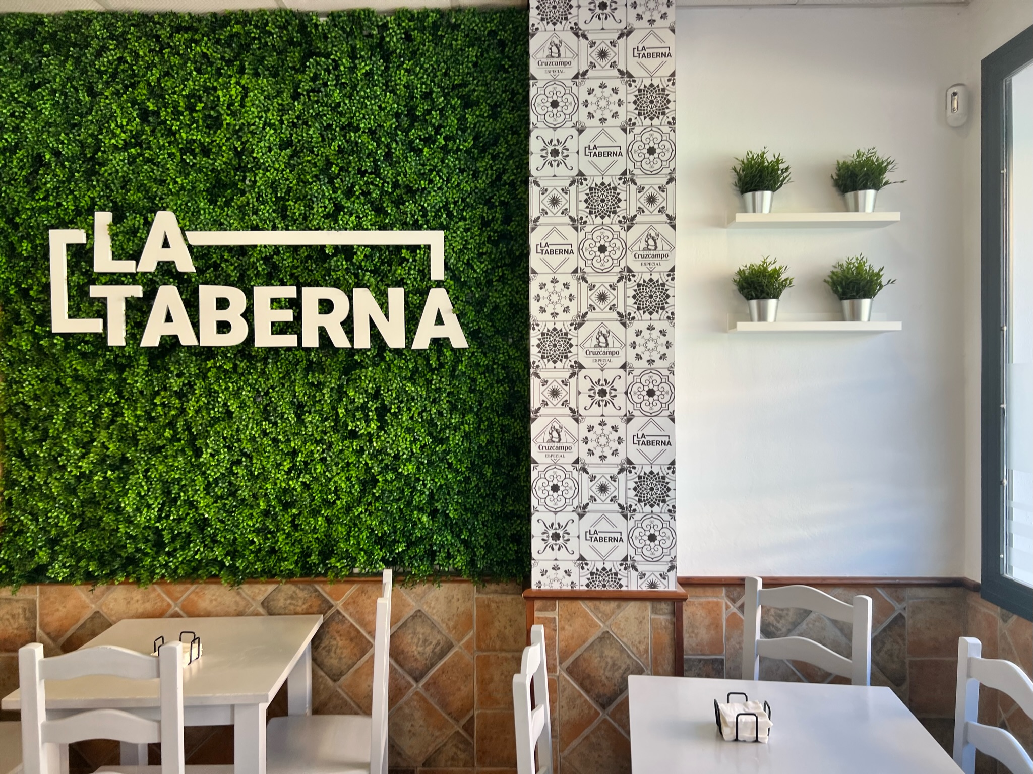 Interior del Bar La Taberna — pared verde con logo, azulejos y mesas blancas